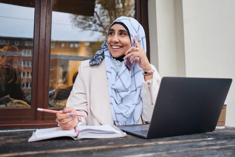 Young smiling Arabic woman in hijab happily talking on smartphon